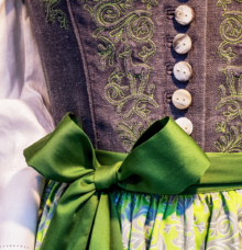 Närbild av en traditionell klänning med gröna broderier och ett grönt band.