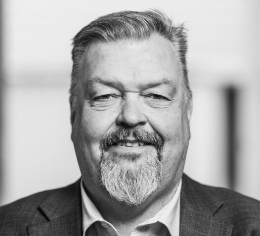 Man med skägg och kostym, ler mot kameran i svartvitt.