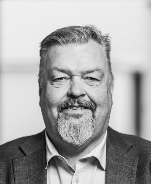 Man med skägg och kostym, ler mot kameran i svartvitt.