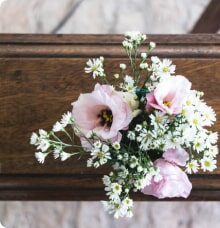 En bukett med ljusrosa blommor och små vita blommor ligger ovanpå en träkista.
