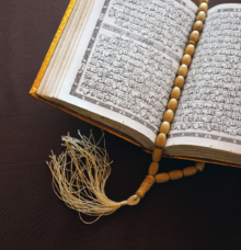 En öppen bok med arabiska tecken och ett radband ovanpå.