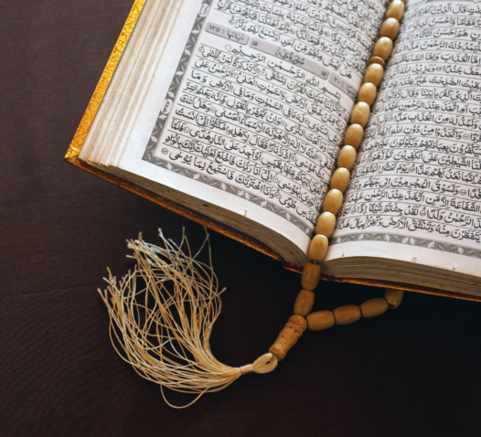 En öppen bok med arabiska tecken och ett radband ovanpå.
