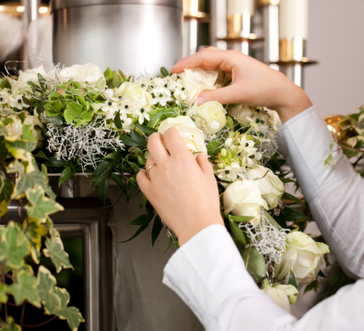 Händer som arrangerar vita rosor och gröna blad i en blomsterdekoration.
