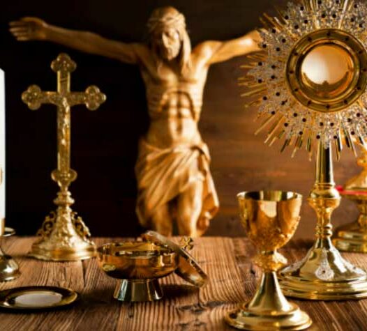 En samling religiösa föremål i guld, inklusive ett krucifix och en monstrans, står på ett bord framför en Jesusstaty.