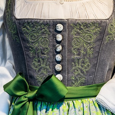 Närbild på en traditionell klänning med broderad korsett och grön rosett.