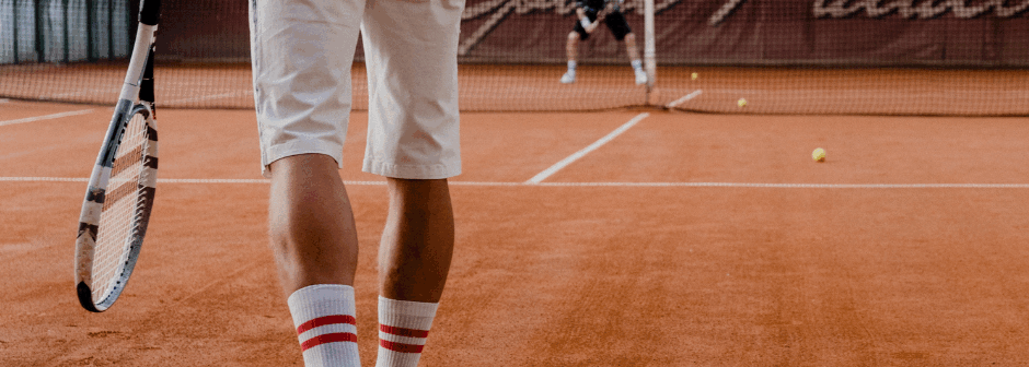 En person i vita shorts och randiga strumpor med en racket på en tennisbana.