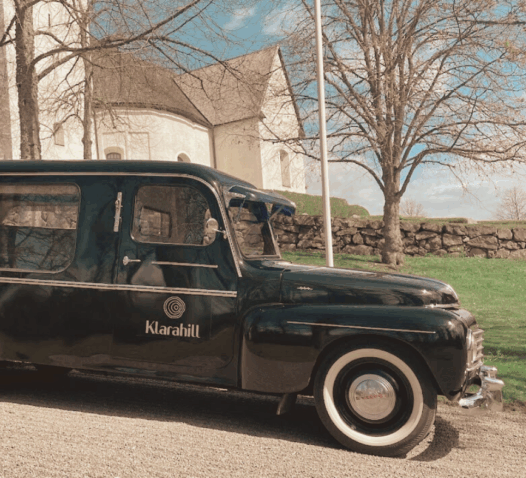 En svart vintage bil med texten "Klasvill" parkerad framför en vit kyrka.