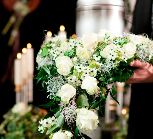 En person håller en begravningskrans av vita blommor framför tända ljus.